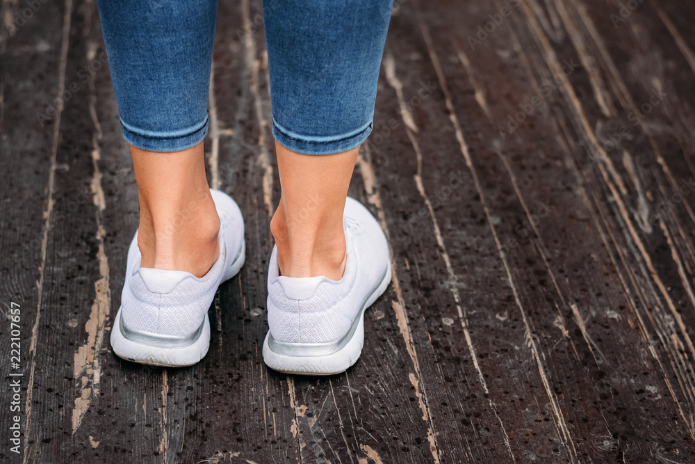 Woman legs in white sneakers on a wooden background