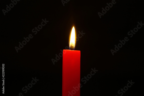 small wax burning red candle with bright flame on the dark background.