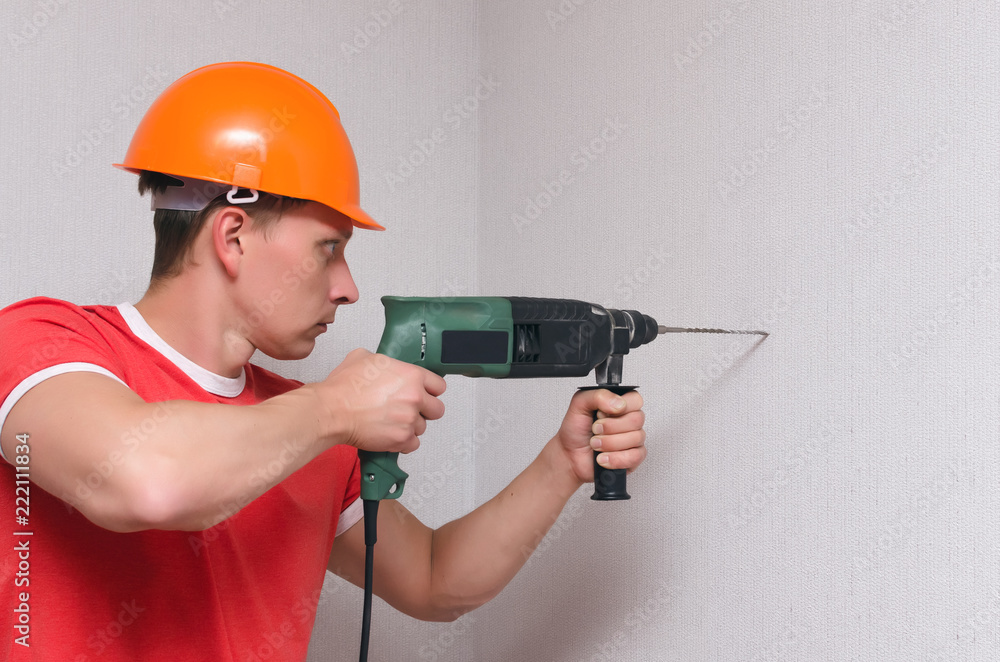 Builder worker drills a wall with a perforator. Home repair concept.