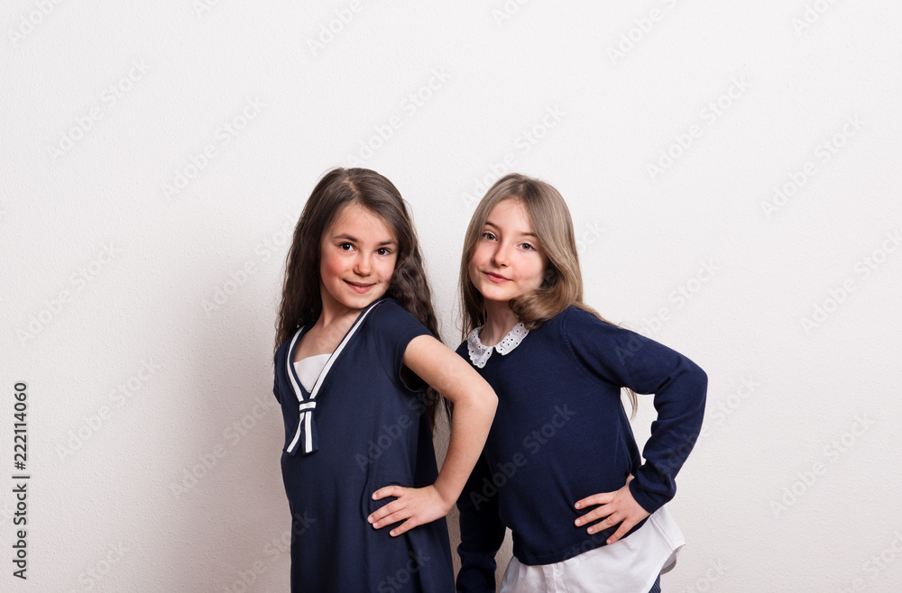 Two small schoolgirls with uniform standing in a studio. Two small schoolgirls with uniform standing in a studio.