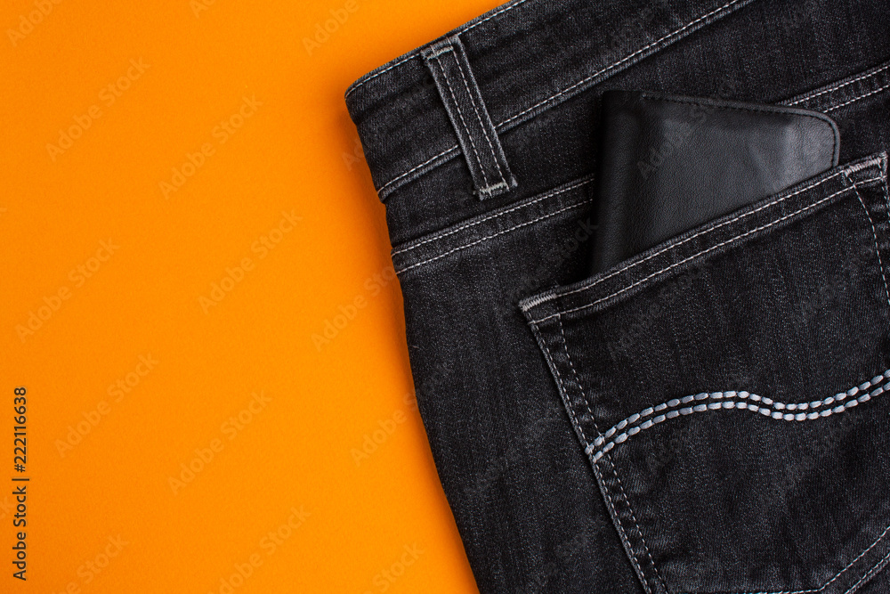 Back pocket of black jeans and black leather wallet on orange background