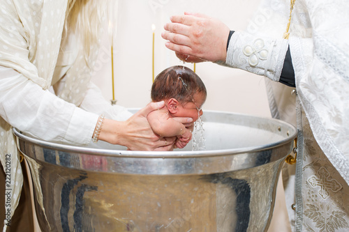 Fotografie, Obraz Mother holds child while priest baptizes with holy water