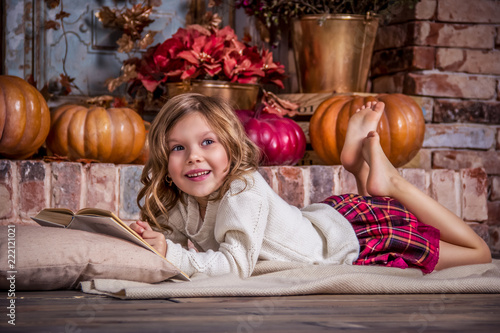 Valokuva Happy little girl is reading book. Happy little girl and pumpkin.