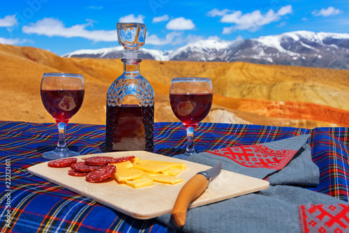 Two glasses of red wine with a decanter, sausage and cheese on a background of a mountain landscape