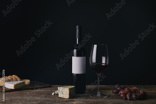 Fototapeta Naklejka Na Ścianę i Meble -  bottle of wine with blank label, glass of red wine, cheese and grapes on wooden table