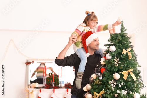 Cute girl with father decorating Christmas tree in room