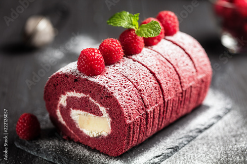 Billede på lærred Red velvet Sponge Swiss roll with fresh raspberry and sugar icing on dark backgr