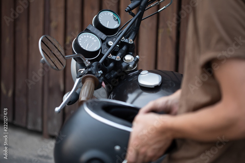 Photography Handsome rider biker guy wearing black helmet and sitting on classic style cafe racer motorcycle