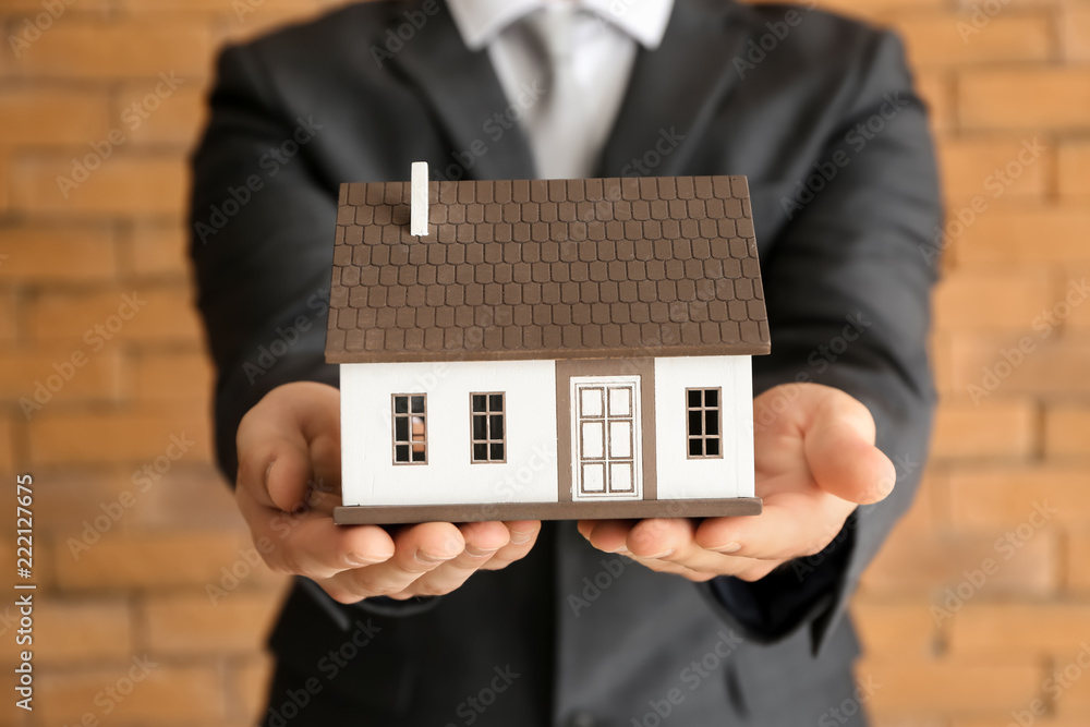 Real estate agent with house model near brick wall, closeup. Mortgage concept Real estate agent with house model near brick wall, closeup. Mortgage concept
