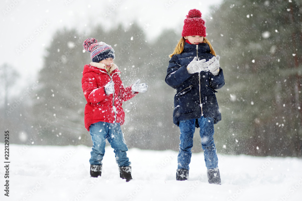 Two adorable little girls having fun together in beautiful winter park. Beautiful sisters playing in a snow. Two adorable little girls having fun together in beautiful winter park. Beautiful sisters playing in a snow.