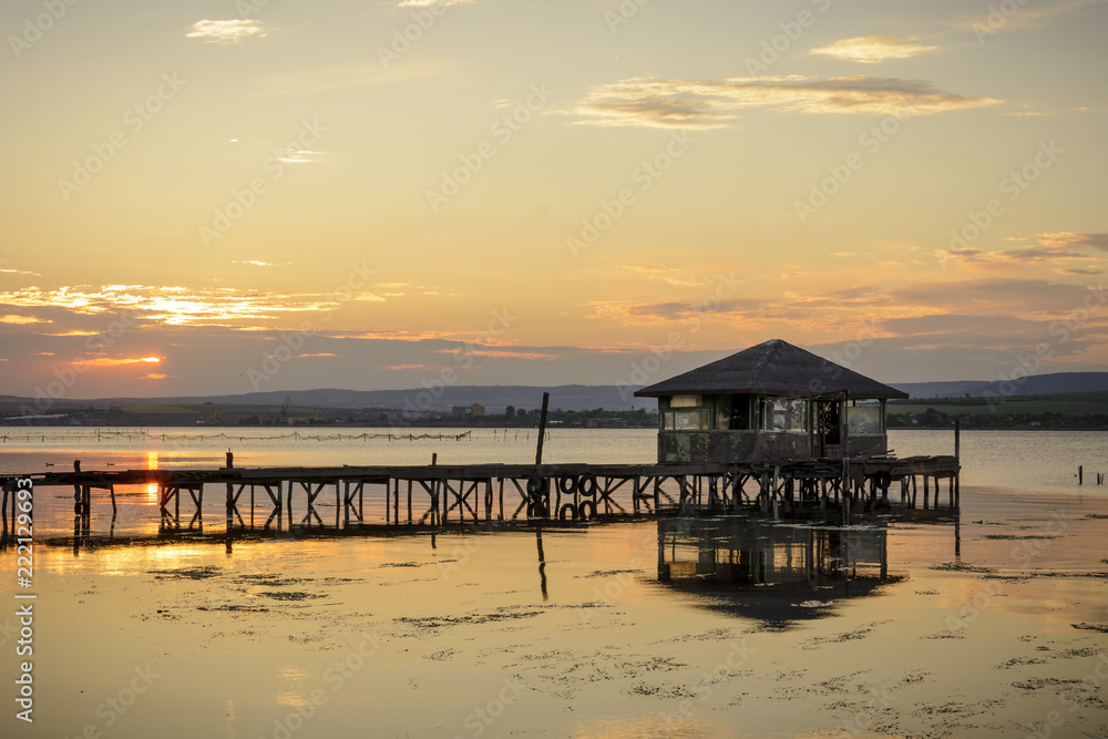 wooden Fishing hut in a lake with pier and fishing net at sunset.