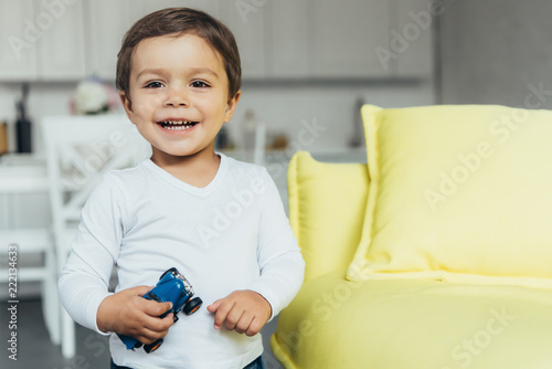 adorable smiling boy holding toy car at home