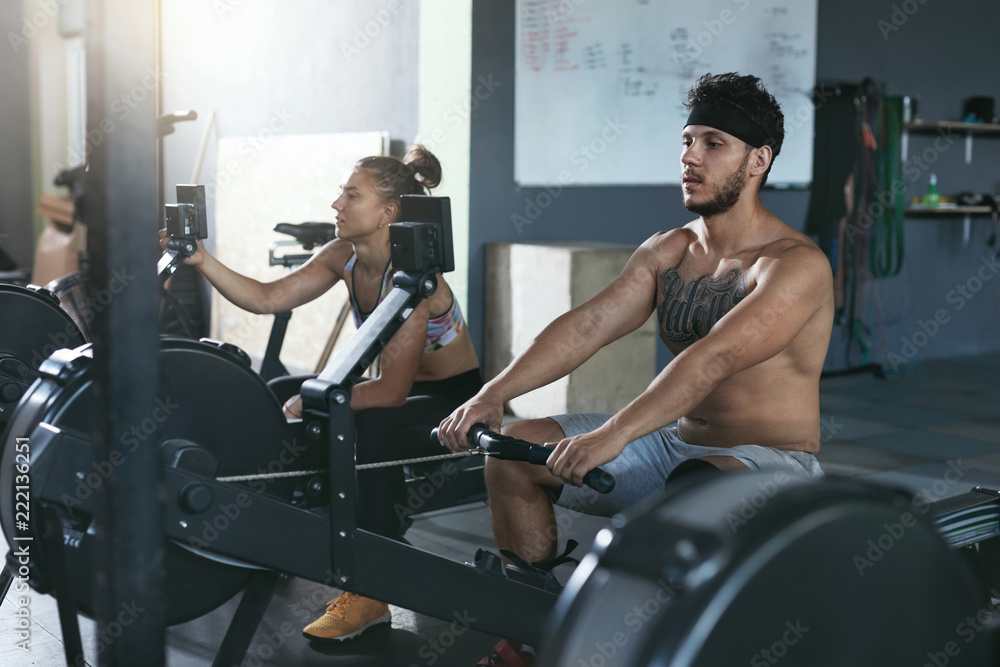 Gym. Man And Woman Training On Rowing Machine At Crossfit Club Gym. Man And Woman Training On Rowing Machine At Crossfit Club