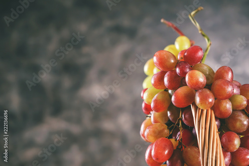Wicker basket with fresh ripe grapes on grey background, closeup
