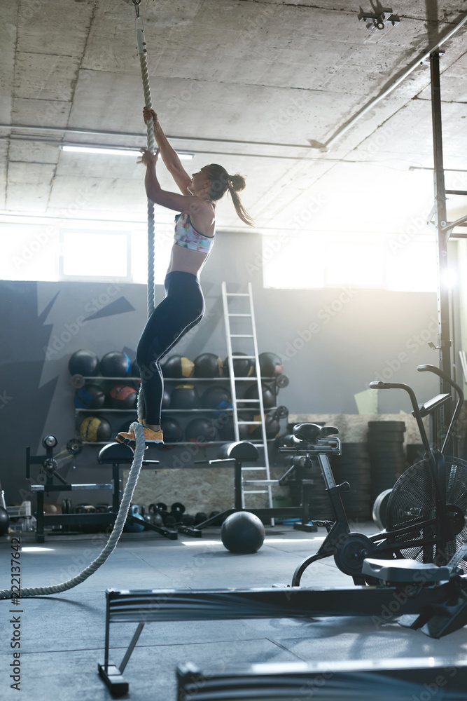 Training At Gym. Female Crossfit Athlete Climbing Rope Stock Photo