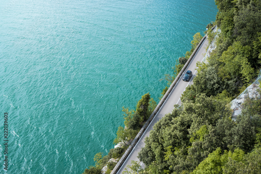 Coastal road between turquoise water and green Mediterranean vegetation, seen from above.