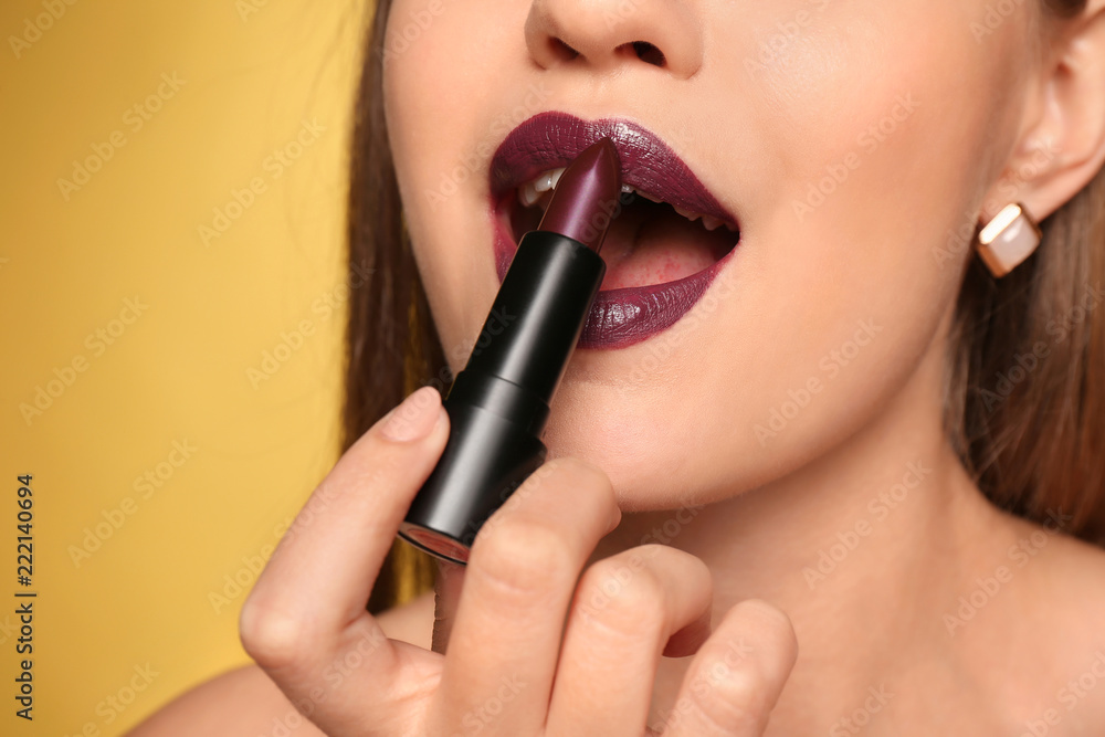 Beautiful young woman applying dark lipstick on color background, closeup Beautiful young woman applying dark lipstick on color background, closeup