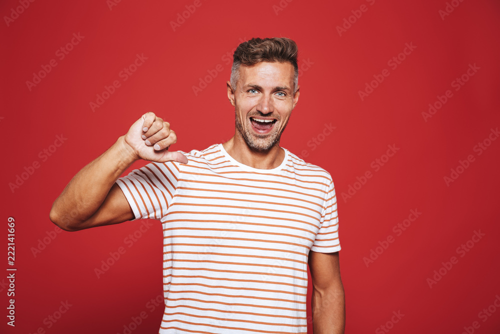 Cheerful man in striped t-shirt showing thumb down with smile, isolated over red background Cheerful man in striped t-shirt showing thumb down with smile, isolated over red background