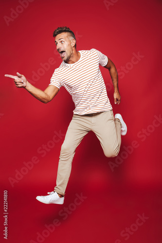 Full length photo of adult man in striped t-shirt running and screaming, isolated over red background