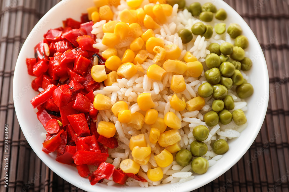 Plate with tasty boiled rice and vegetables on bamboo mat Plate with tasty boiled rice and vegetables on bamboo mat