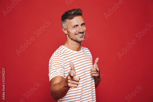 Caucasian man 30s in striped t-shirt gesturing index finger on camera meaning hey you, isolated over red background photo