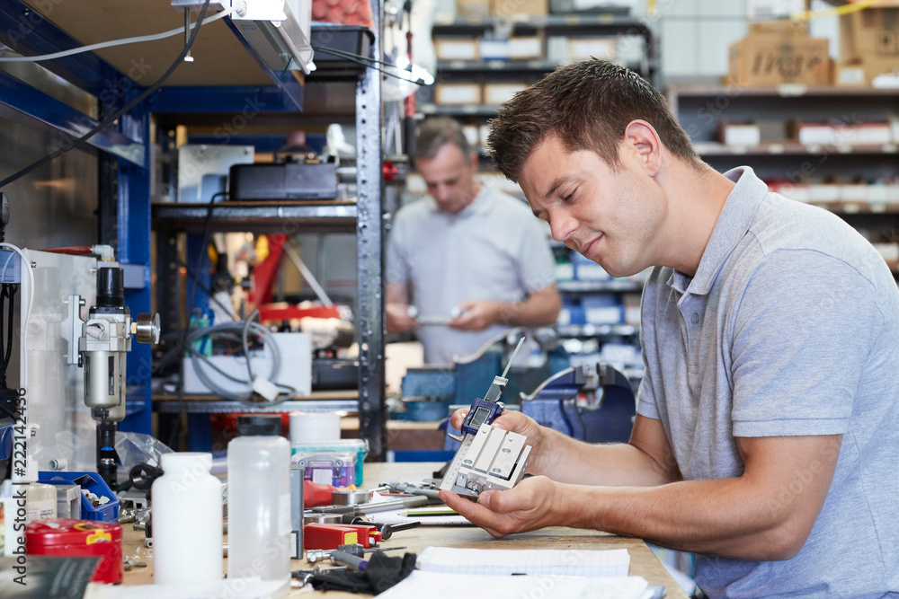 Fototapeta premium Engineer In Factory Measuring Component At Work Bench Using Micrometer
