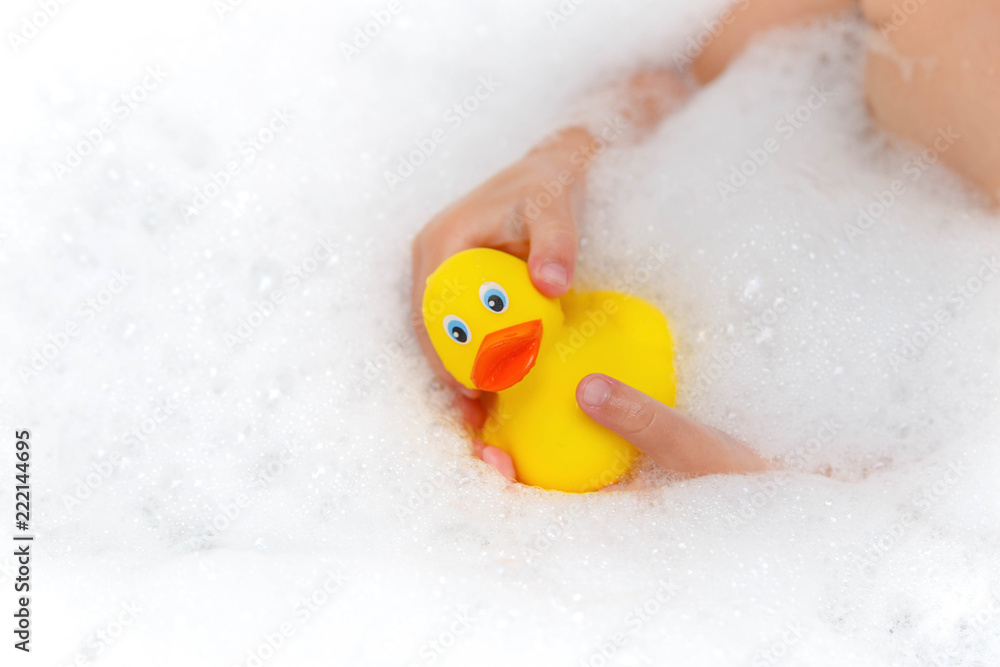 Child playing with toy rubber duck in bath with soap foam. Baby hands with rubber duck isolated on white. Child playing with toy rubber duck in bath with soap foam. Baby hands with rubber duck isolated on white.