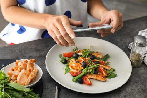 Woman taking photo of chicken salad with mobile phone at table