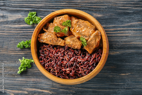 Bowl with tasty boiled rice and meat on wooden table
