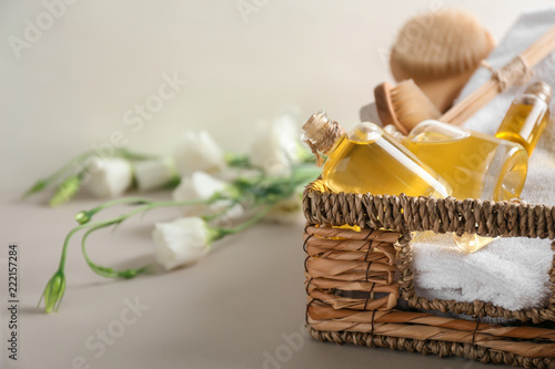 Bottles with essential oil and towel in wicker basket on grey table