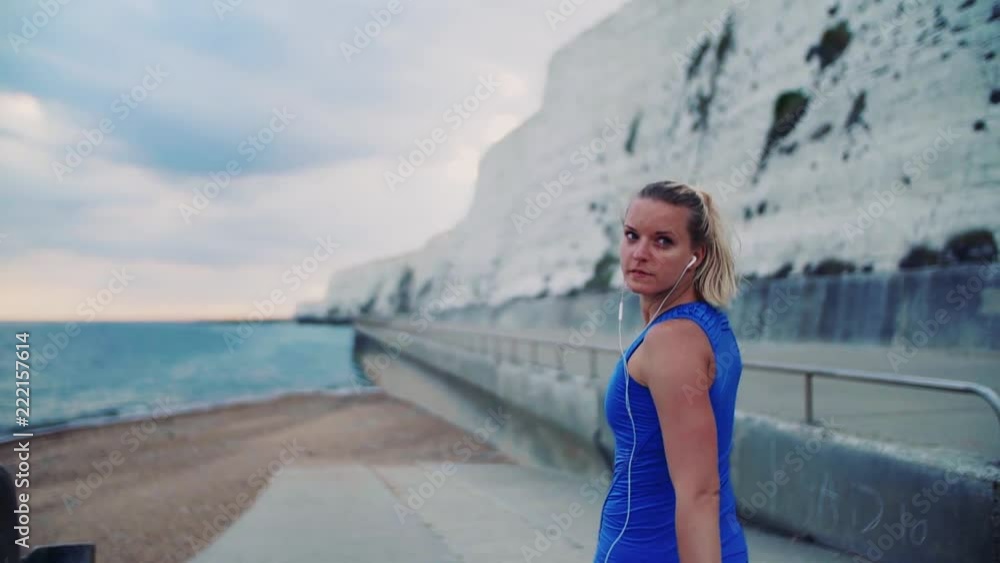 Young sporty woman runner with earphones walking on the beach outside. Young sporty woman runner with earphones walking on the beach outside.