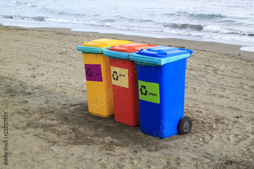 multi-colored containers for sorting garbage are on the beach against the sea