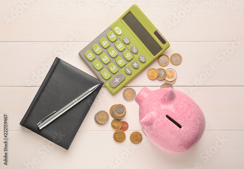 Cute piggy bank with coins, notebook and calculator on wooden table
