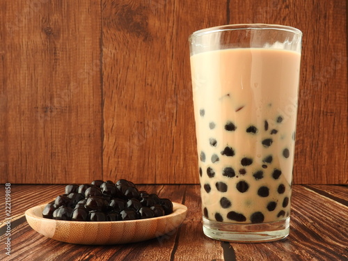A glass cup of pearl milk tea (also called bubble tea) and a plate of tapioca ball on wooden background. Pearl milk tea is the most representative drink in Taiwan. Taiwan food . With copy space.