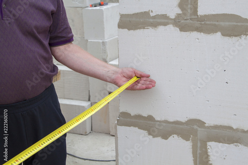 Close up view of the hand holding the measuring tape next to the foam block. The customer measures the width and length of the building under construction.