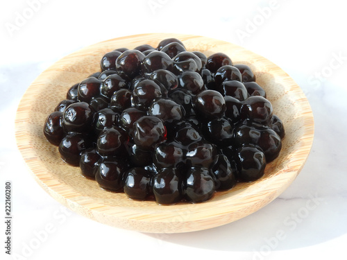 High angle view of tapioca ball (also known as boba in bubble tea) on wooden plate isolated on white background. Ingredients for making pearl milk tea and shaved ice at dessert shop. Food concept.