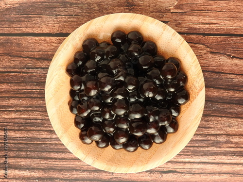 Top view of tapioca ball (also known as boba in bubble tea) on wooden plate isolated on wooden background. It is ingredients for making pearl milk tea and shaved ice at dessert shop. Food concept.