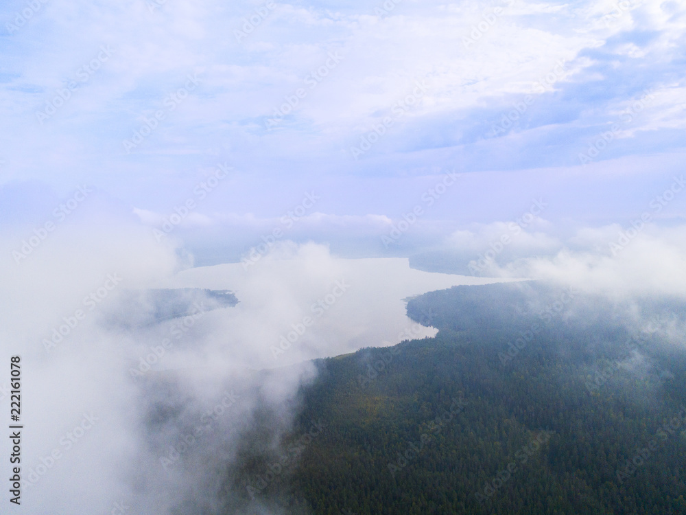 Aerial Drone view clouds over the green forest and lake. Low lying cloud. Aerial view of over tropical rainforest. Above the clouds in the sky. Big clouds. Atmosphere. Top view from drone