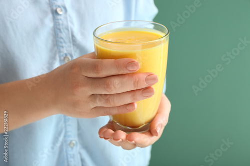 Woman holding glass of tasty yellow smoothie on color background, closeup