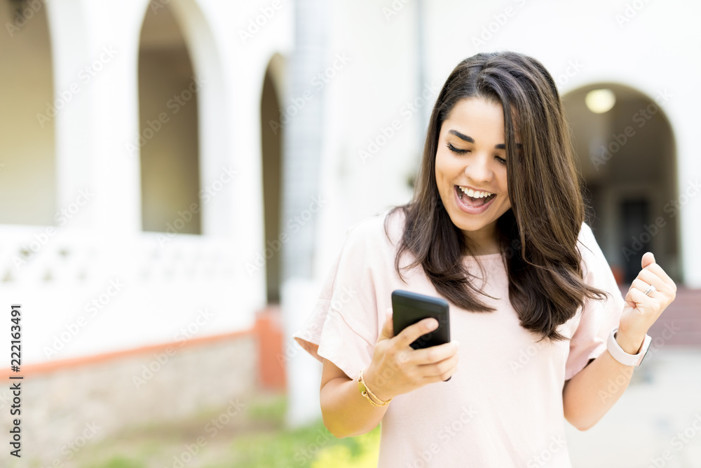 Woman Receiving Good News On Smartphone Outdoors