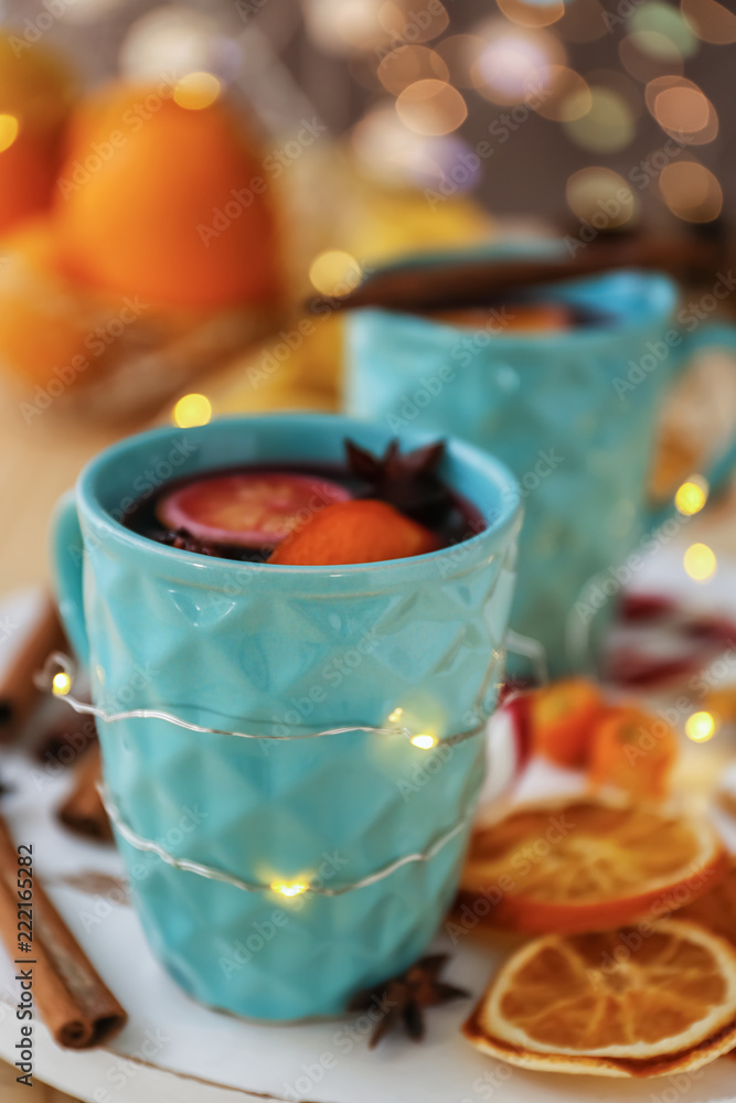Cup of delicious mulled wine with Christmas garland on table
