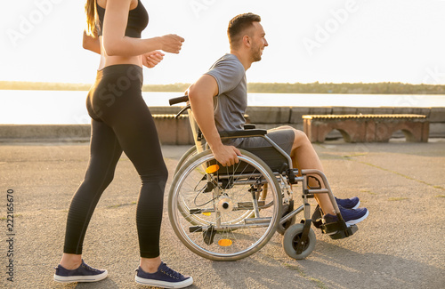 Young man in wheelchair and sporty woman training outdoors