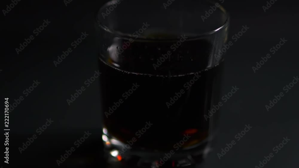 Ice cubes fall into a glass with cola Ice cubes fall into a glass with cola