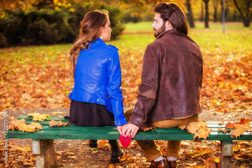 Couple holding heart-shape on a bench in the park.