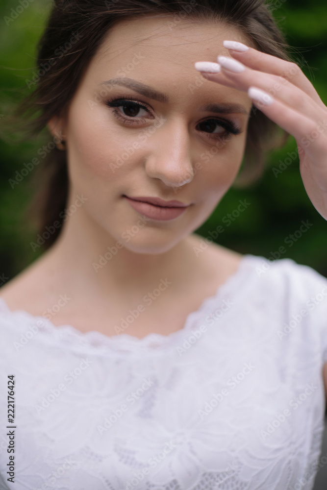 Naklejka premium Close up portrait of young tender bride woman with nude make up in white wedding dress outdors in the park. Wedding concept