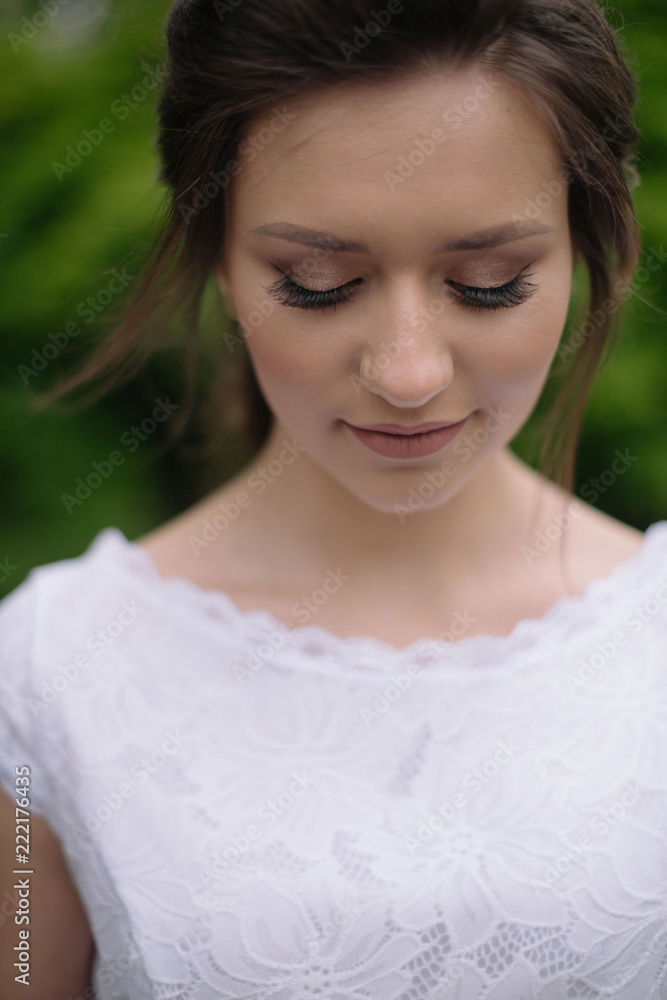 Portrait of young beautiful bride woman with nude make up in white wedding dress lookimg down outdors in the park. Wedding concept. Close up Portrait of young beautiful bride woman with nude make up in white wedding dress lookimg down outdors in the park. Wedding concept. Close up