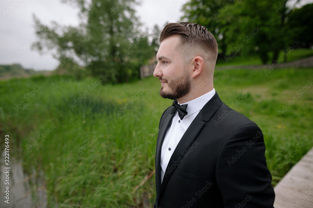 Close up young handsome groom in elegant suit walking on the pier near the lake on wedding day. Wedding ceremony Close up young handsome groom in elegant suit walking on the pier near the lake on wedding day. Wedding ceremony