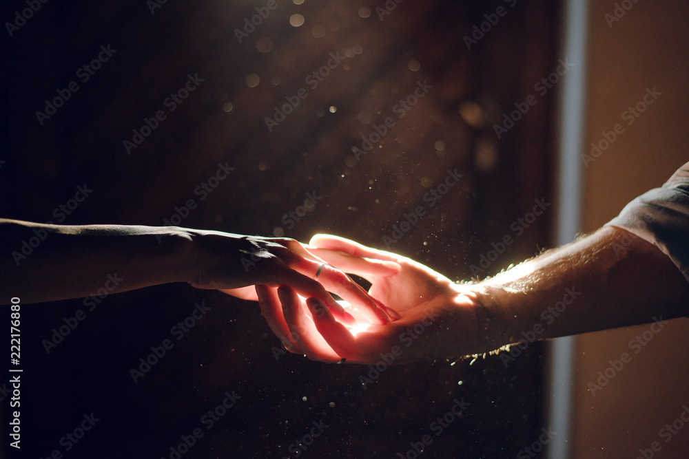 Wedding couple hands. Man and woman holding hands in the dark on the sun ray. Close up