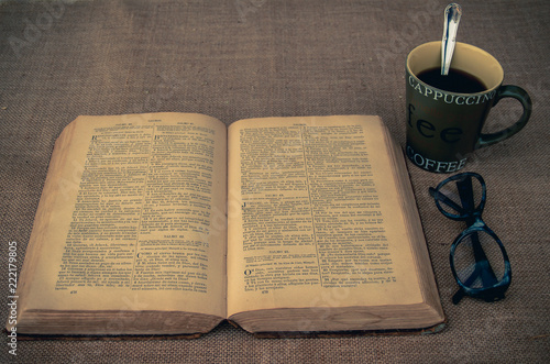 Vintage style. open antique book with eye glasses, cup of coffee and burlap background photo