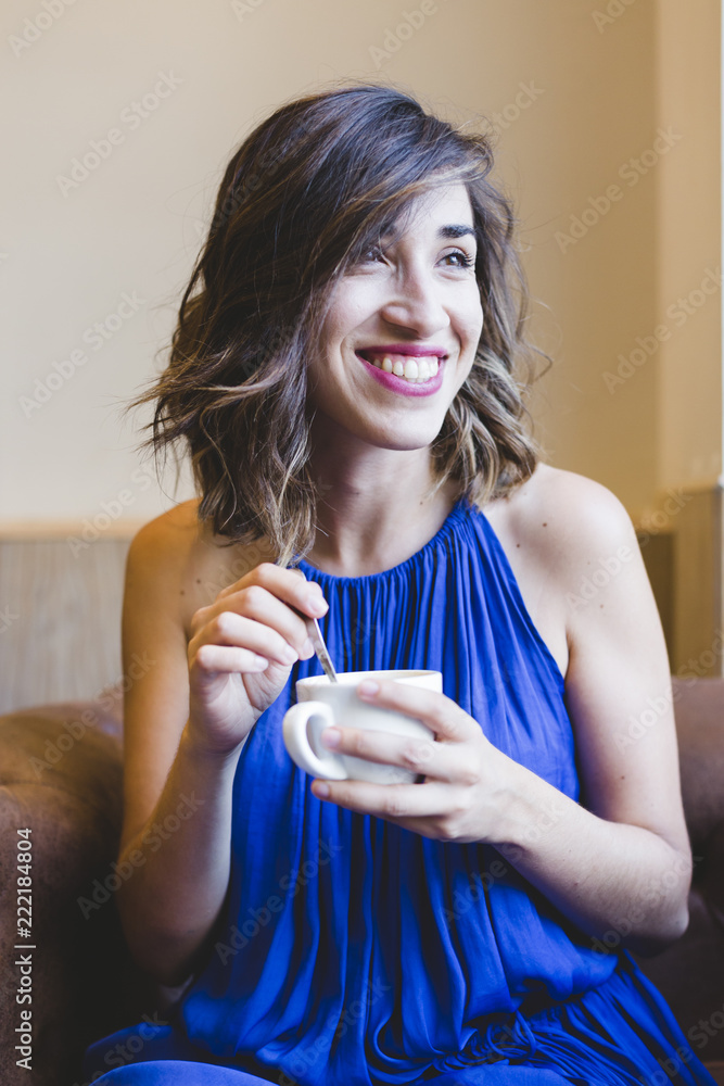 young beautiful woman enjoying a cup of coffee in a cafe. laptop besides. Casual blue dress. Modern life indoors young beautiful woman enjoying a cup of coffee in a cafe. laptop besides. Casual blue dress. Modern life indoors